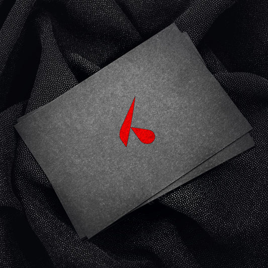 Pila di cartoline nere personalizzate con il logo K rosso, quella in primo piano leggermente inclinata, su un tessuto scuro