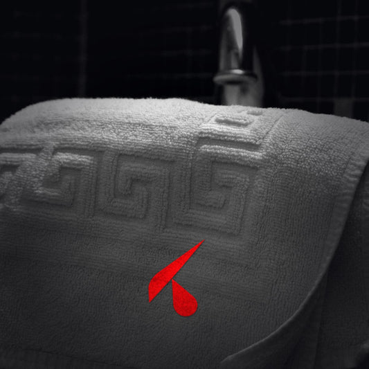 Asciugamano bianco d'albergo con logo K rosso ricamato, piegato sul bordo del lavabo in un bagno scuro