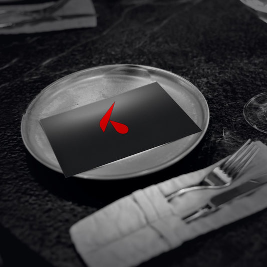 Menù plastificato nero con logo K rosso in testa, appoggiato su un piatto di un tavolo di ristorante con tovagliolo, posate e calice