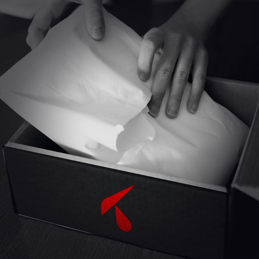 Scatola nera semiaperta con carta velina bianca e logo K rosso stampato sul fronte, su un bancone scuro