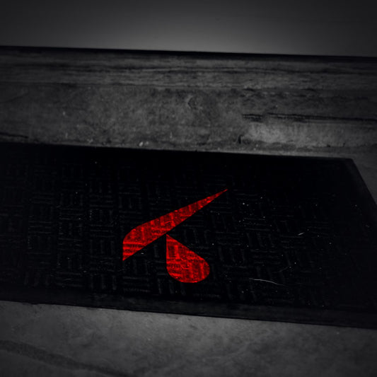 Zerbino nero con logo K rosso stampato, davanti alla porta d'ingresso di un negozio